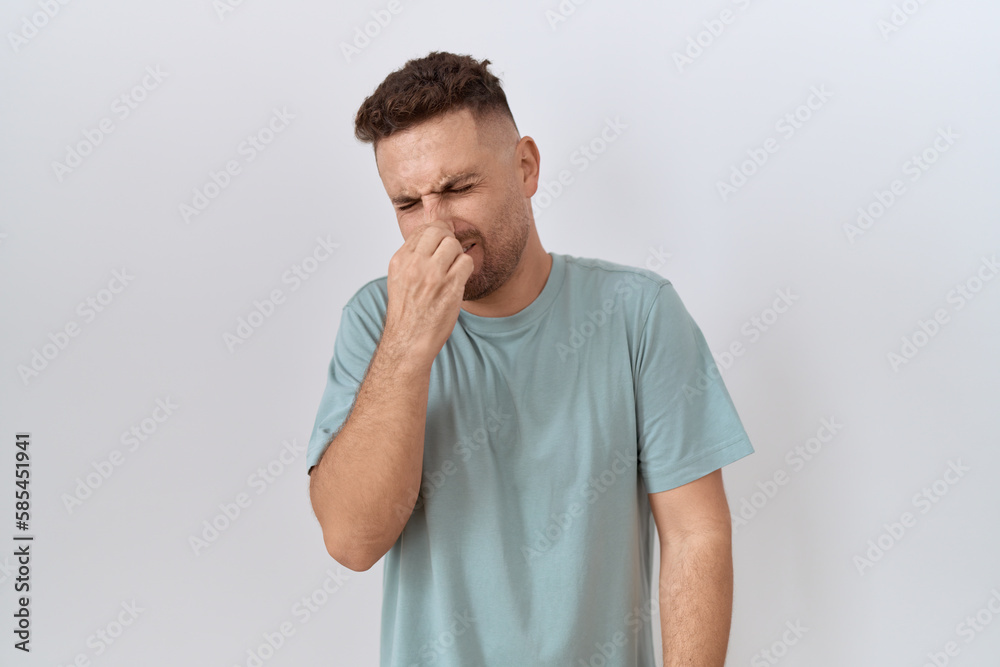 Hispanic man with beard standing over white background smelling something stinky and disgusting, intolerable smell, holding breath with fingers on nose. bad smell Hispanic man with beard standing over white background smelling something stinky and disgusting, intolerable smell, holding breath with fingers on nose. bad smell
