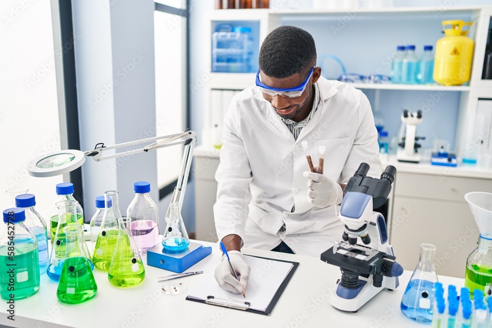 Young african american man wearing scientist uniform writing on clipboard holding test tubes at laboratory Young african american man wearing scientist uniform writing on clipboard holding test tubes at laboratory