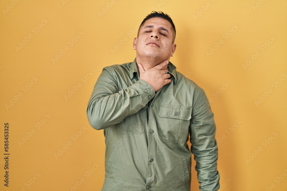 Hispanic young man standing over yellow background touching painful neck, sore throat for flu, clod and infection Hispanic young man standing over yellow background touching painful neck, sore throat for flu, clod and infection