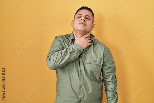 Hispanic young man standing over yellow background touching painful neck, sore throat for flu, clod and infection