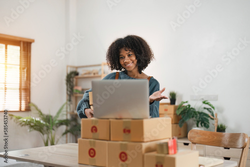 Portrait of Starting small businesses SME owners, African American woman video call check online orders Selling products working with box freelance work at home office © Natee Meepian