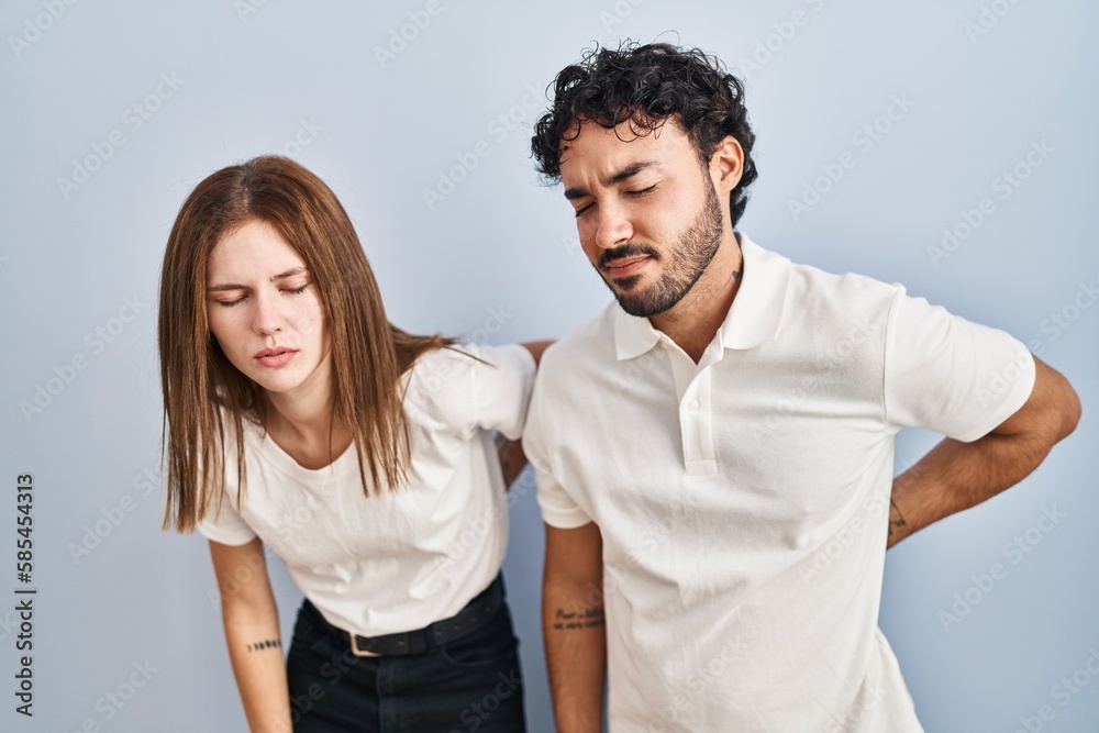 Young couple wearing casual clothes standing together suffering of backache, touching back with hand, muscular pain Young couple wearing casual clothes standing together suffering of backache, touching back with hand, muscular pain