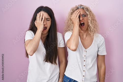 Mother and daughter standing together over pink background yawning tired covering half face, eye and mouth with hand. face hurts in pain.