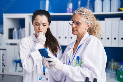 Two women scientists using smartphone working at laboratory