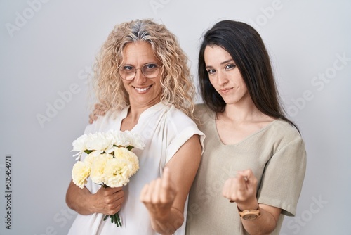 Mother and daughter holding bouquet of white flowers beckoning come here gesture with hand inviting welcoming happy and smiling