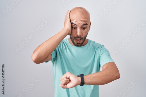 Middle age bald man standing over white background looking at the watch time worried, afraid of getting late