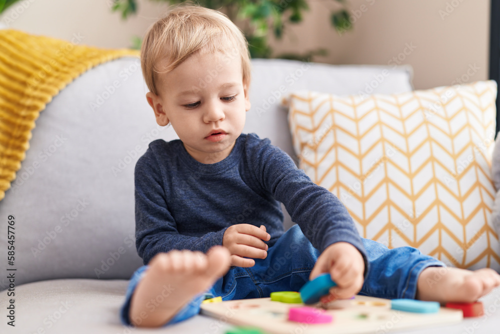 Adorable blond toddler playing with maths game sitting on sofa at home Adorable blond toddler playing with maths game sitting on sofa at home