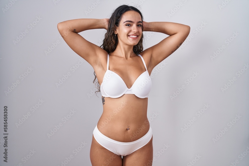 Fototapeta premium Young hispanic woman wearing white lingerie relaxing and stretching, arms and hands behind head and neck smiling happy