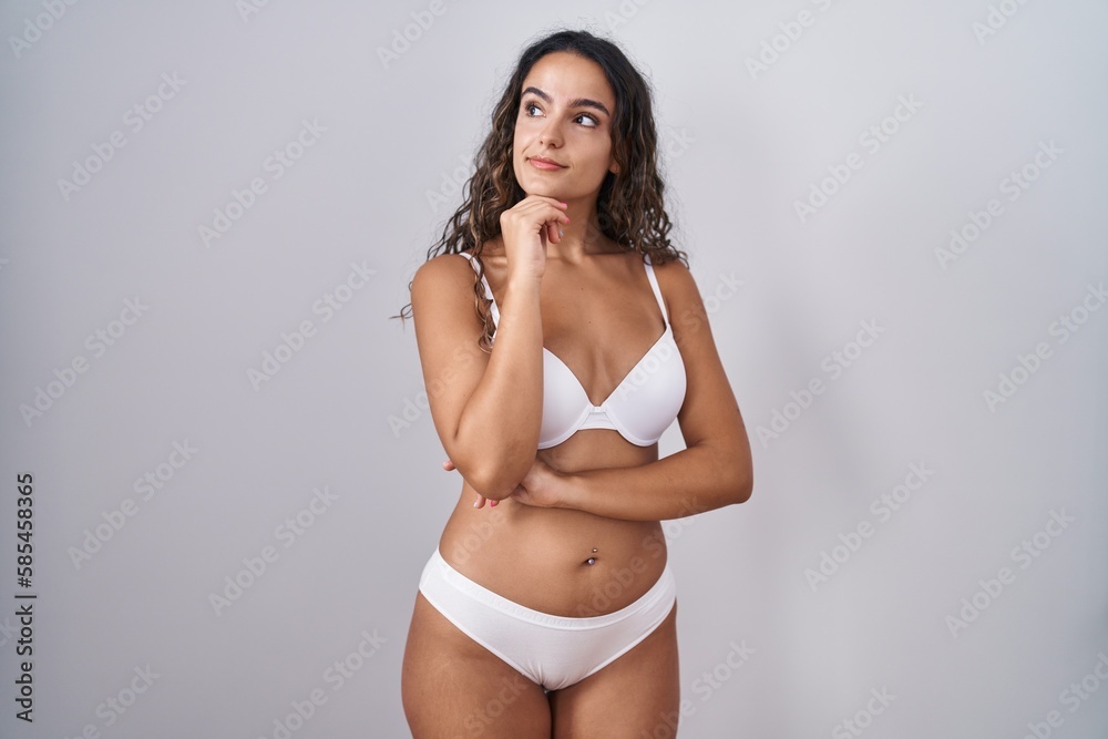 Young hispanic woman wearing white lingerie with hand on chin thinking about question, pensive expression. smiling with thoughtful face. doubt concept. Young hispanic woman wearing white lingerie with hand on chin thinking about question, pensive expression. smiling with thoughtful face. doubt concept.