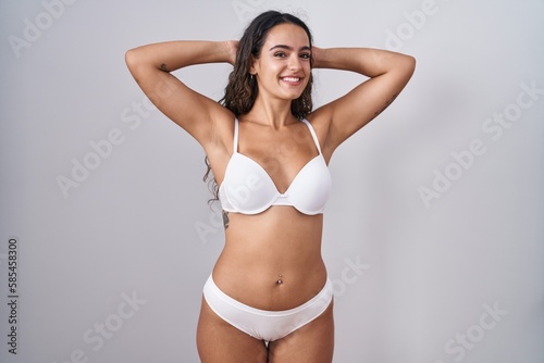 Young hispanic woman wearing white lingerie relaxing and stretching, arms and hands behind head and neck smiling happy