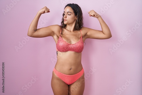 Young hispanic woman wearing lingerie over pink background showing arms muscles smiling proud. fitness concept.