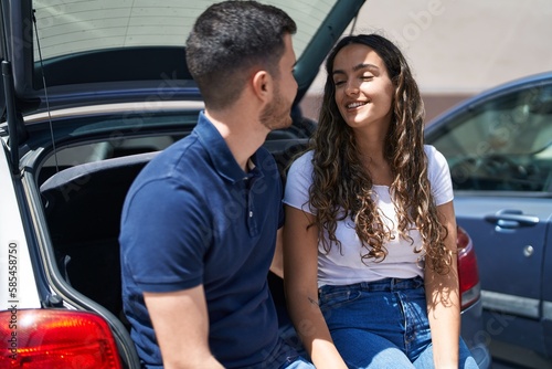 Young hispanic couple sitting on car trunk together at street