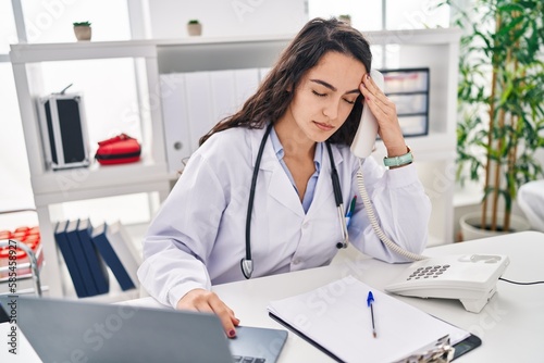 Young hispanic woman wearing doctor uniform worried working at clinic