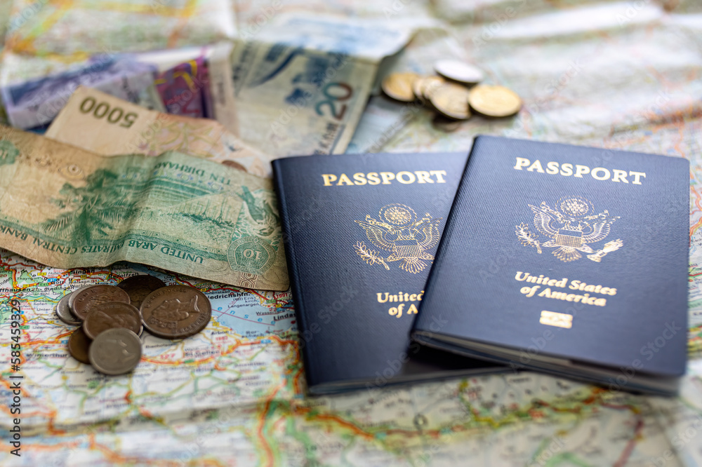 two US American passports laying on large road map of foreign country close-up with foreign currency bills and coins two US American passports laying on large road map of foreign country close-up with foreign currency bills and coins
