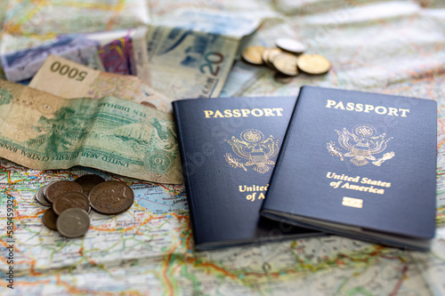two US American passports laying on large road map of foreign country close-up with foreign currency bills and coins