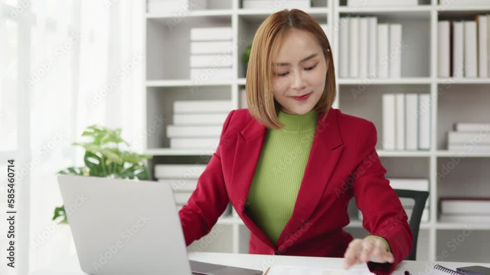 Businesswoman in red suit working on laptop and paperwork that show cost planning accounting numbers tables on office space. Businesswoman in red suit working on laptop and paperwork that show cost planning accounting numbers tables on office space.