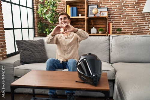 Young man wearing cervical collar for motorbike accident smiling in love showing heart symbol and shape with hands. romantic concept.