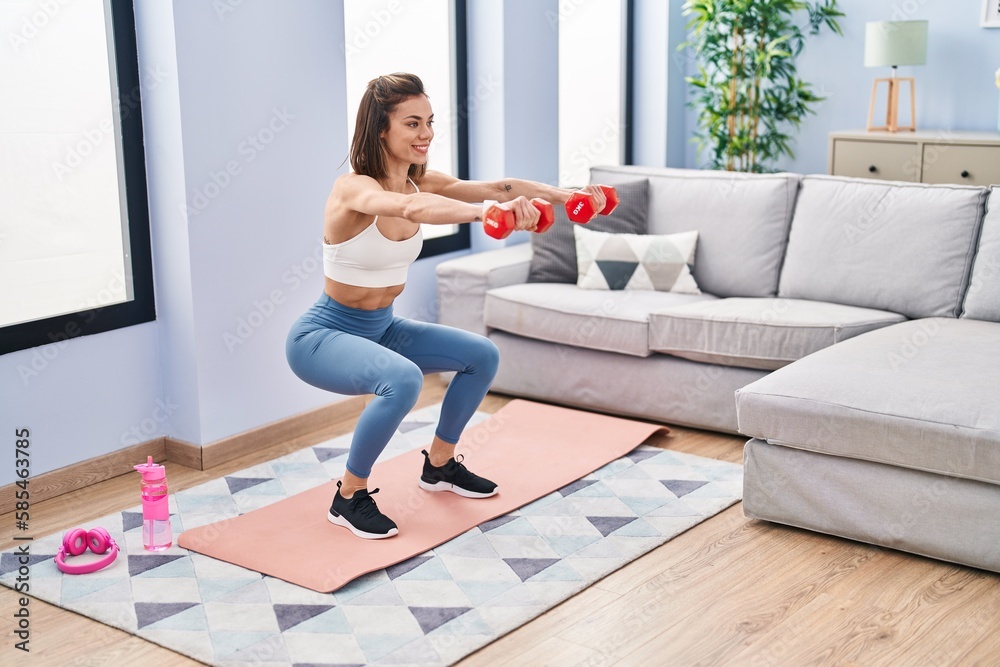 Young beautiful hispanic woman training leg exercise using dumbbells at home Young beautiful hispanic woman training leg exercise using dumbbells at home