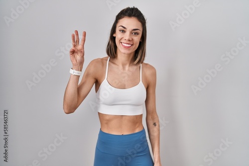 Hispanic woman wearing sportswear over isolated background showing and pointing up with fingers number three while smiling confident and happy. © Krakenimages.com