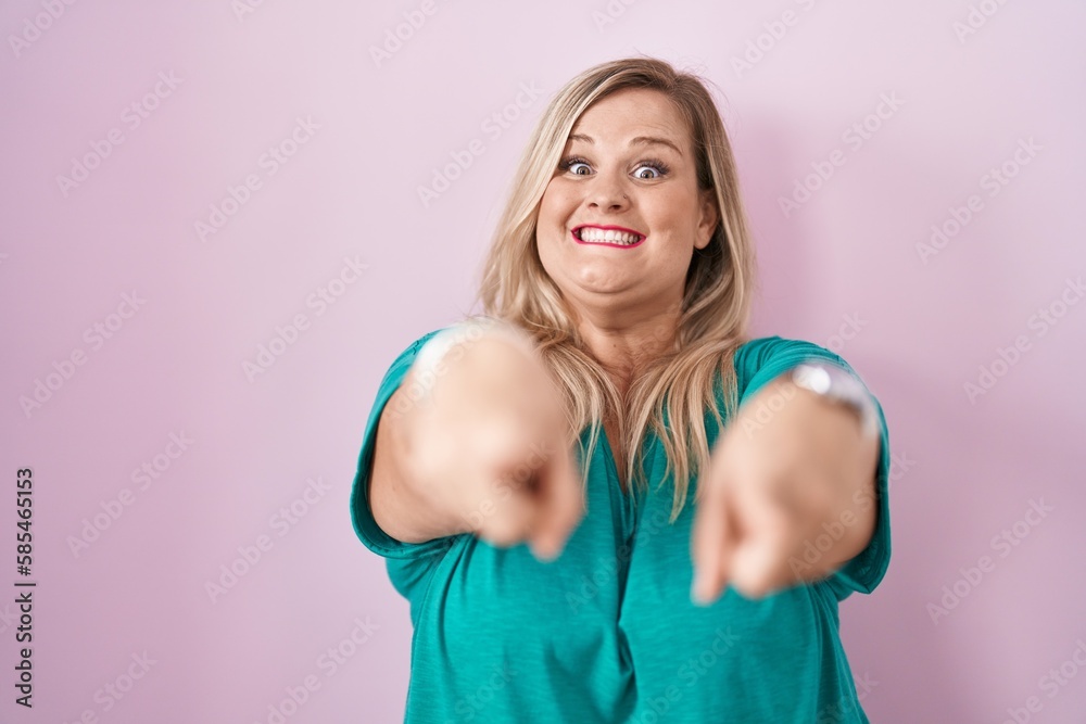 Caucasian plus size woman standing over pink background pointing to you and the camera with fingers, smiling positive and cheerful Caucasian plus size woman standing over pink background pointing to you and the camera with fingers, smiling positive and cheerful