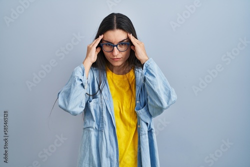 Young hispanic woman standing over blue background with hand on head, headache because stress. suffering migraine.