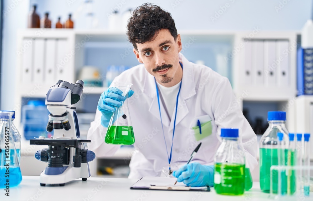 Young caucasian man scientist writing report holding test tube at laboratory
