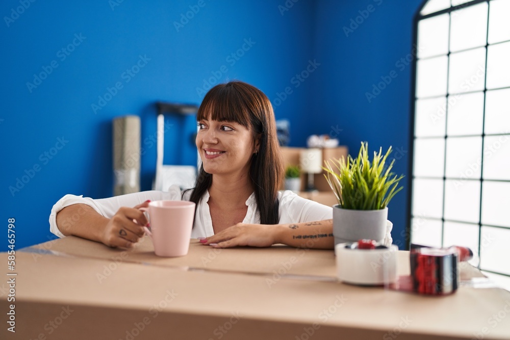 Young beautiful hispanic woman drinking coffee leaning on package at new home Young beautiful hispanic woman drinking coffee leaning on package at new home