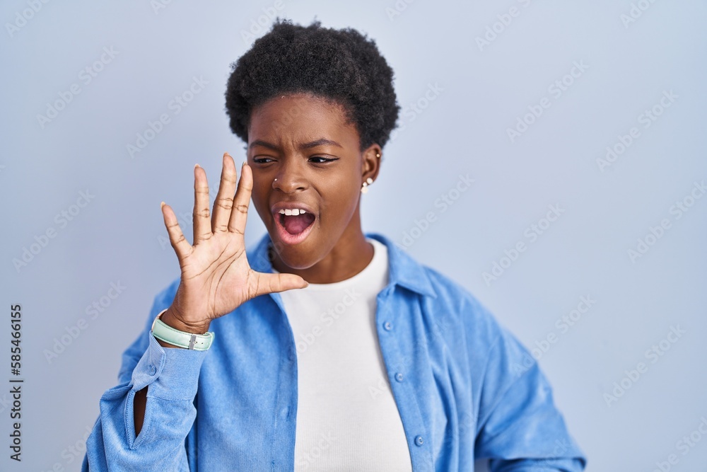 African american woman standing over blue background shouting and screaming loud to side with hand on mouth. communication concept. African american woman standing over blue background shouting and screaming loud to side with hand on mouth. communication concept.