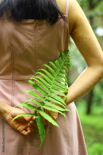 A Woman holding a small piece of fern on her back © Thanha