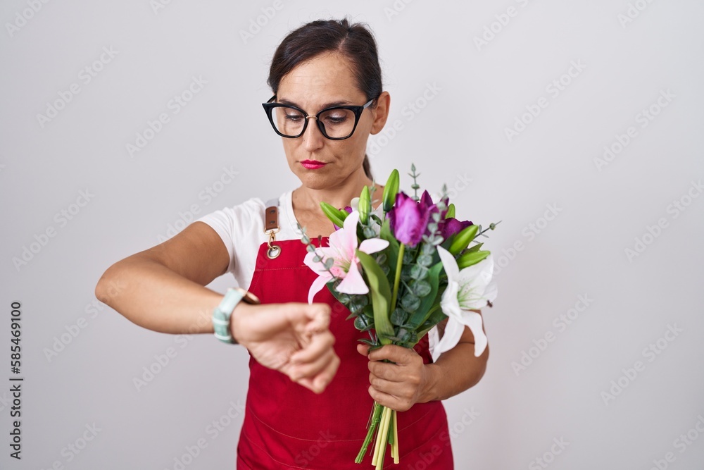 Middle age brunette woman wearing apron working at florist shop holding bouquet checking the time on wrist watch, relaxed and confident Middle age brunette woman wearing apron working at florist shop holding bouquet checking the time on wrist watch, relaxed and confident