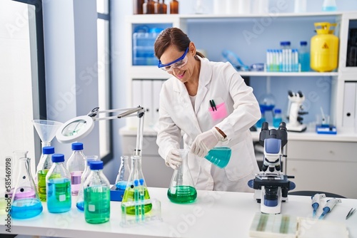 Middle age woman wearing scientist uniform pouring liquid at laboratory
