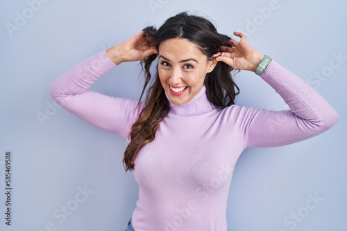 Young brunette woman standing over blue background smiling pulling ears with fingers, funny gesture. audition problem © Krakenimages.com
