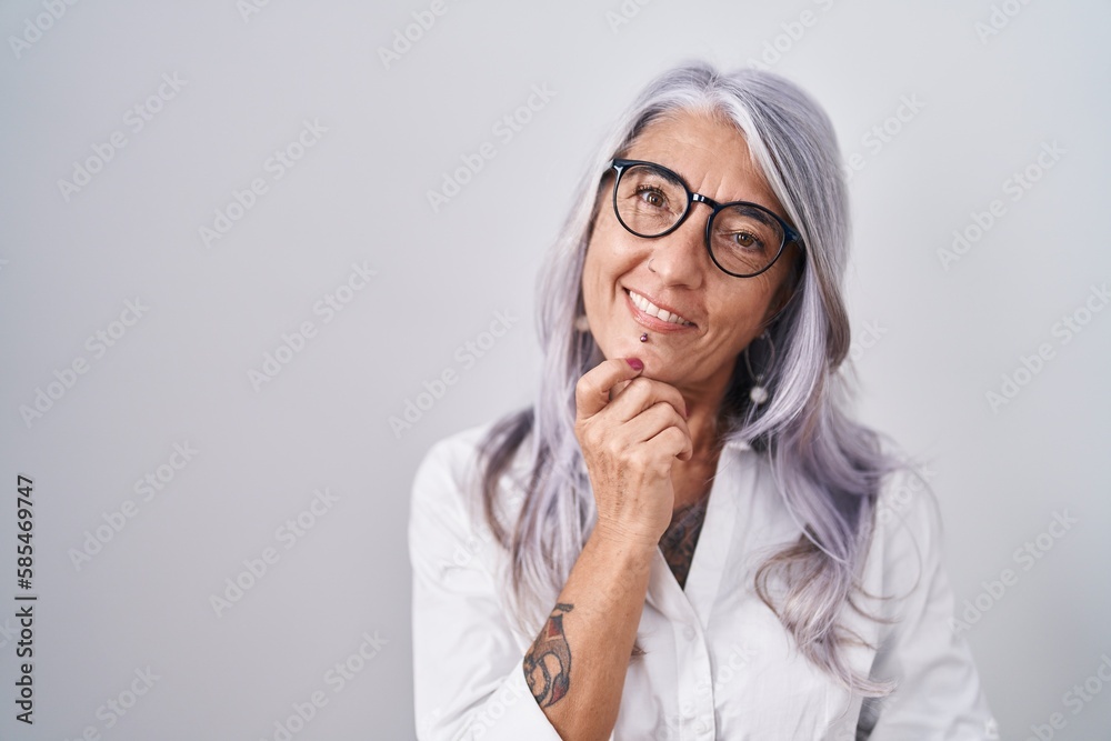 Middle age woman with tattoos wearing glasses standing over white background looking confident at the camera smiling with crossed arms and hand raised on chin. thinking positive.