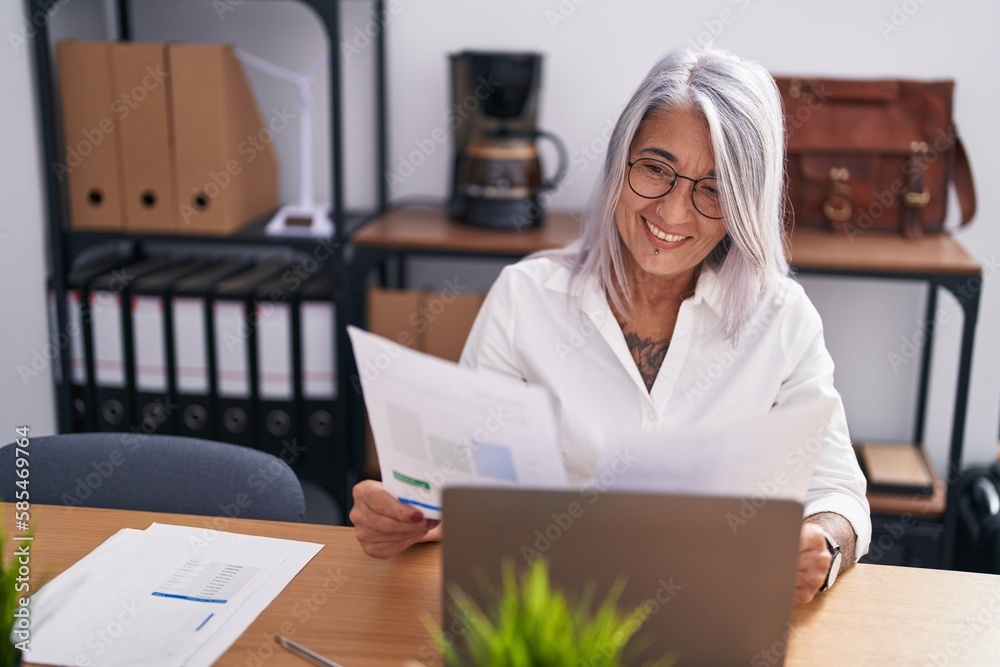 Middle age grey-haired woman business worker using laptop reading document at office Middle age grey-haired woman business worker using laptop reading document at office