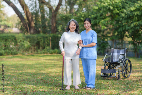 Asian nurse or female caregiver helping senior woman holding cane to walk in the hospital garden.