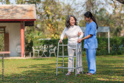 Asian nurse or a female physiotherapist is helping an elderly woman patient use a walker to learn to walk.