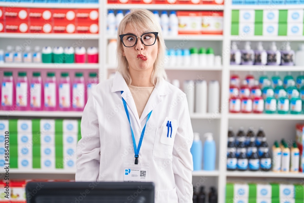 Young caucasian woman working at pharmacy drugstore making fish face with lips, crazy and comical gesture. funny expression.
