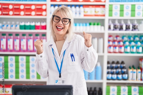 Young caucasian woman working at pharmacy drugstore very happy and excited doing winner gesture with arms raised, smiling and screaming for success. celebration concept.