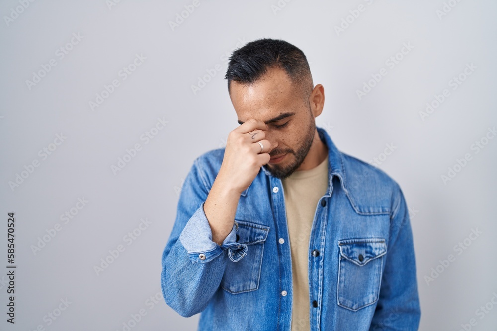 Young hispanic man standing over isolated background tired rubbing nose and eyes feeling fatigue and headache. stress and frustration concept. Young hispanic man standing over isolated background tired rubbing nose and eyes feeling fatigue and headache. stress and frustration concept.