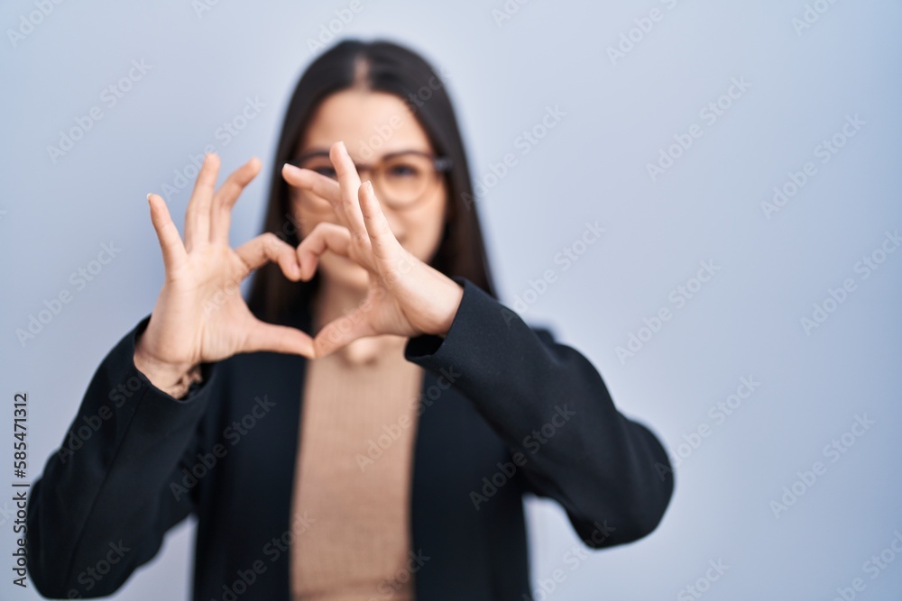Young brunette woman standing over blue background smiling in love doing heart symbol shape with hands. romantic concept. Young brunette woman standing over blue background smiling in love doing heart symbol shape with hands. romantic concept.