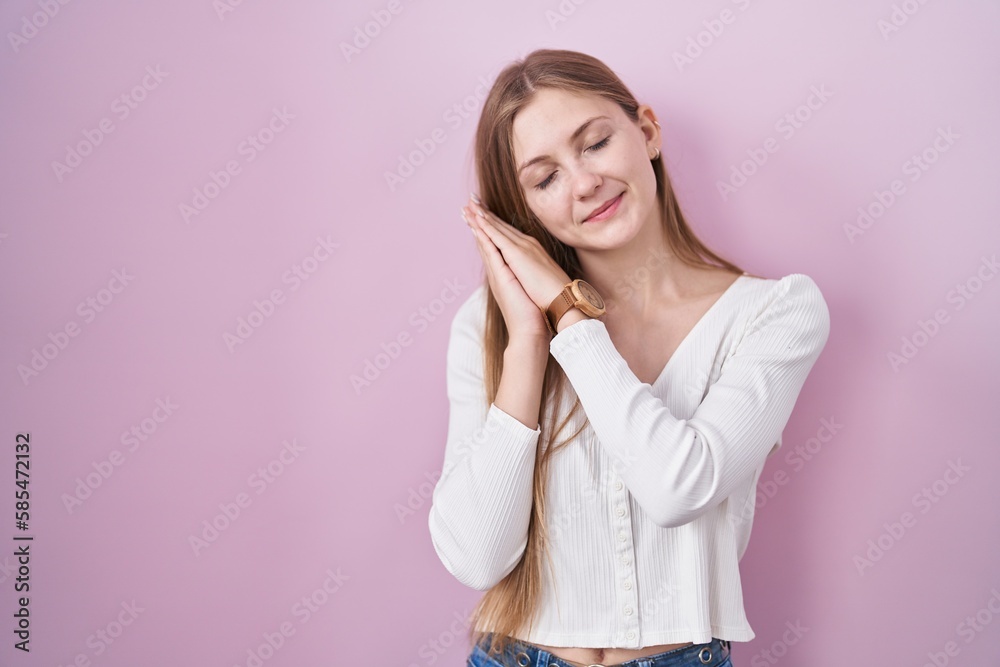 Young caucasian woman standing over pink background sleeping tired dreaming and posing with hands together while smiling with closed eyes. Young caucasian woman standing over pink background sleeping tired dreaming and posing with hands together while smiling with closed eyes.