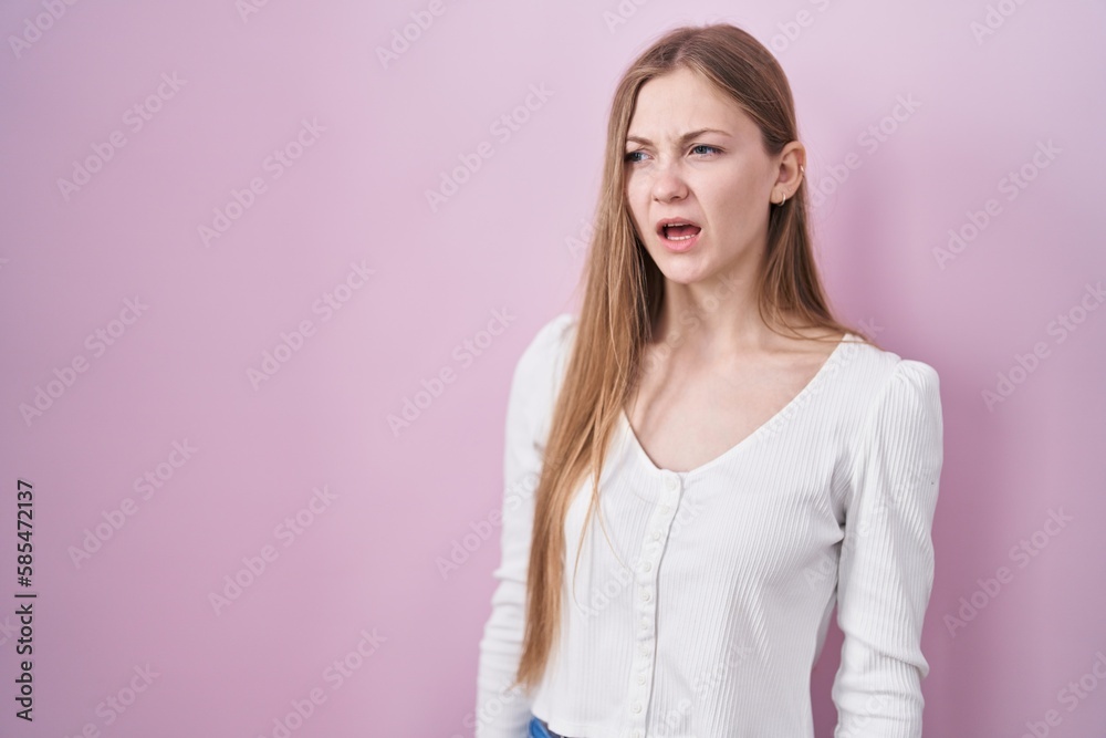 Young caucasian woman standing over pink background angry and mad screaming frustrated and furious, shouting with anger. rage and aggressive concept. Young caucasian woman standing over pink background angry and mad screaming frustrated and furious, shouting with anger. rage and aggressive concept.