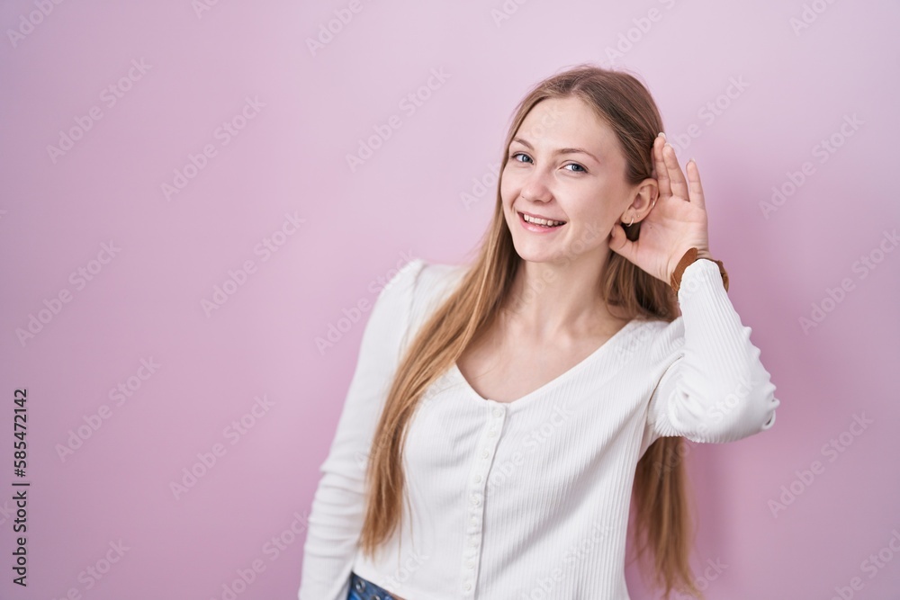 Young caucasian woman standing over pink background smiling with hand over ear listening an hearing to rumor or gossip. deafness concept. Young caucasian woman standing over pink background smiling with hand over ear listening an hearing to rumor or gossip. deafness concept.