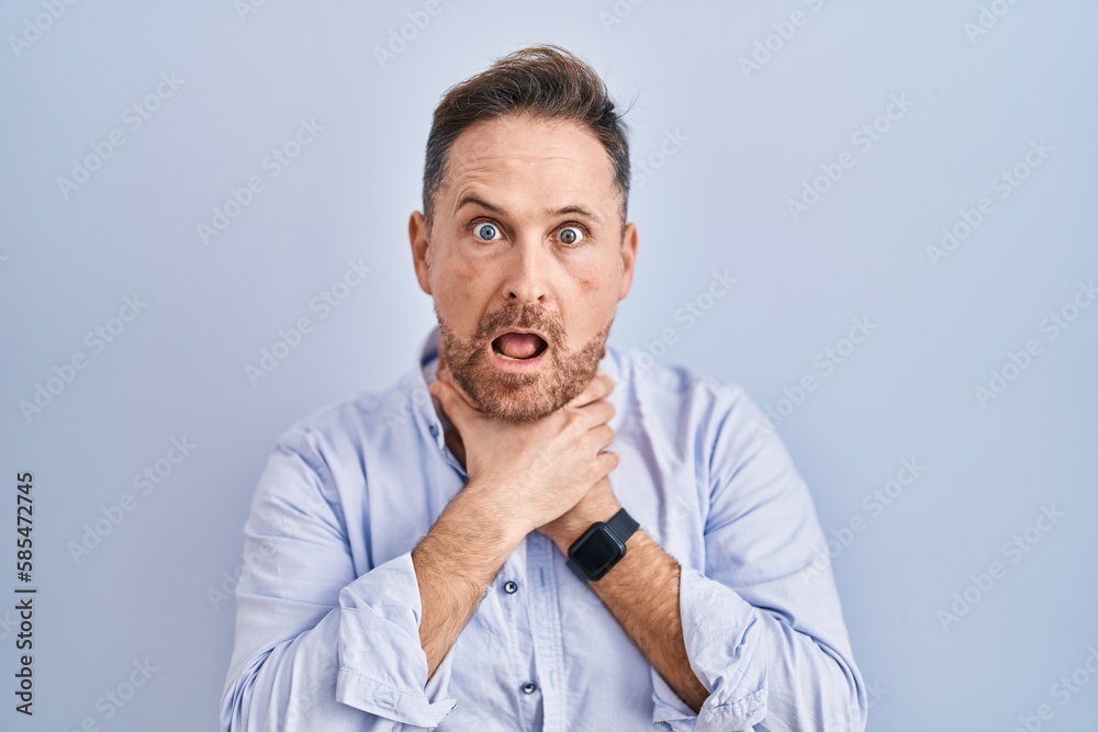 Middle age caucasian man standing over blue background shouting suffocate because painful strangle. health problem. asphyxiate and suicide concept.