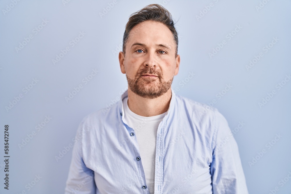 Middle age caucasian man standing over blue background relaxed with serious expression on face. simple and natural looking at the camera. Middle age caucasian man standing over blue background relaxed with serious expression on face. simple and natural looking at the camera.