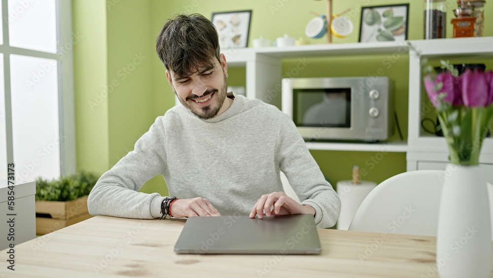 Young hispanic man opening laptop at dinning room Young hispanic man opening laptop at dinning room