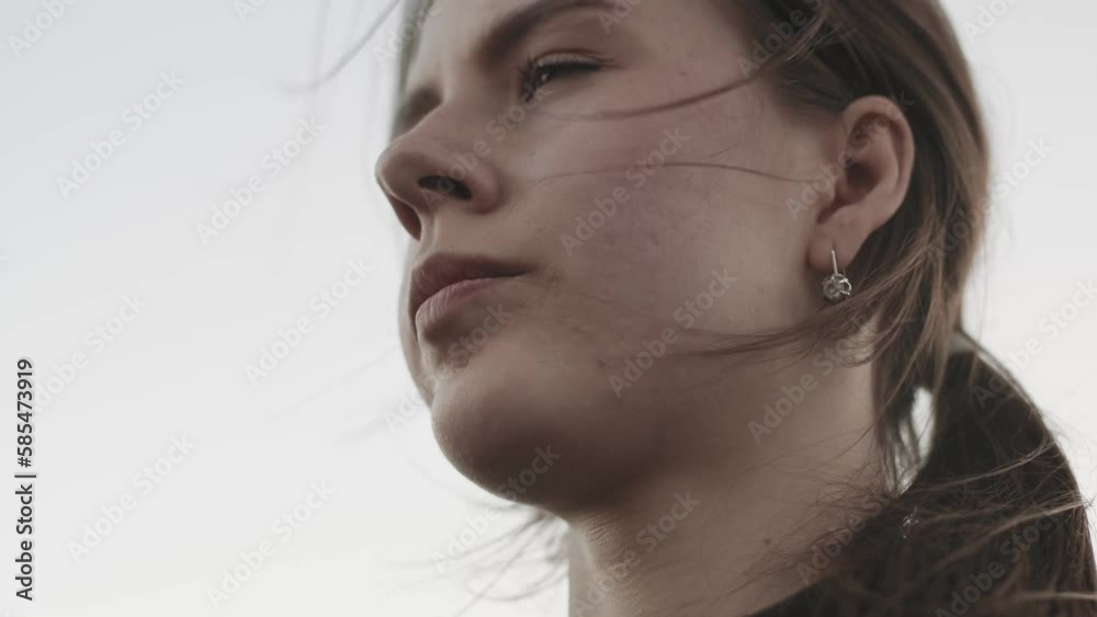 Young beautiful woman dreamily looking into the distance close up. Attractive woman with long brown hair blowing in the wind on a clear sunny day