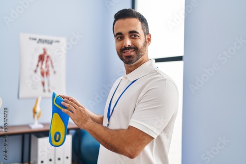 Young hispanic man podiatrist holding insole at podiatry center photo