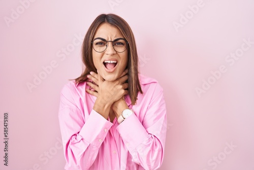 Young hispanic woman wearing glasses standing over pink background shouting suffocate because painful strangle. health problem. asphyxiate and suicide concept. © Krakenimages.com