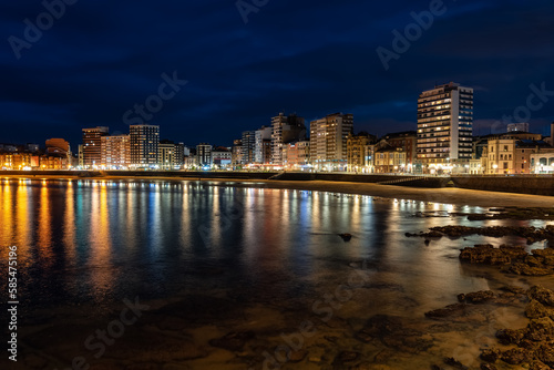 Promenade at night with reflections of lights and buildings in the sea water, Gijon, Asturias.